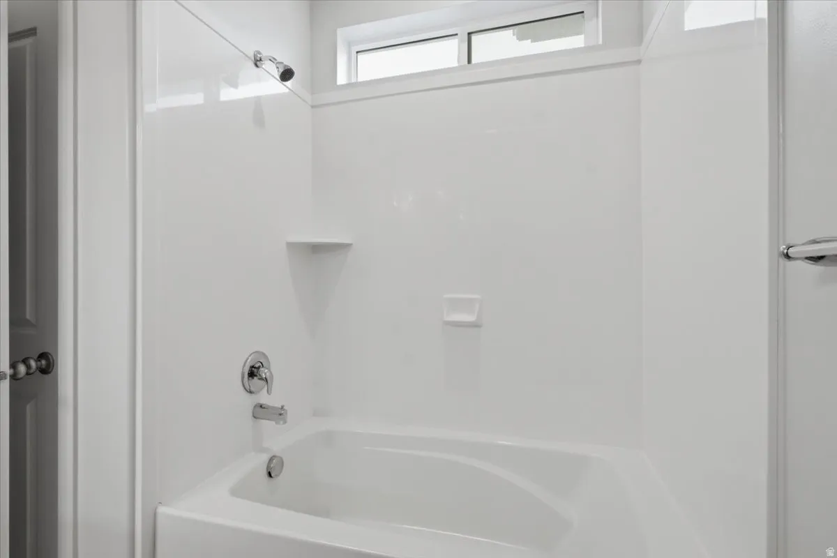 White acrylic bathtub and shower surround with chrome fixtures, an integrated soap dish, and a transom window