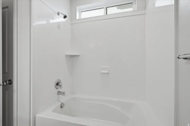 White acrylic bathtub and shower surround with chrome fixtures, an integrated soap dish, and a transom window