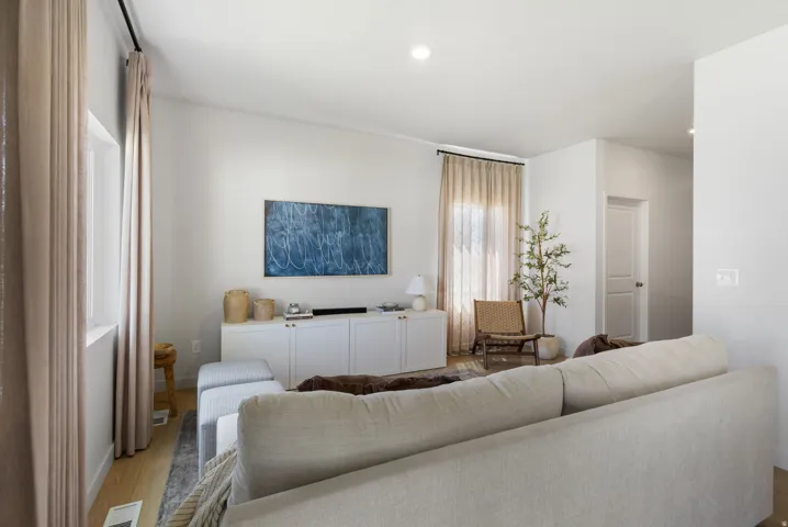 Light wood-finish flooring, recessed lighting, white built-in cabinetry, and a window with neutral drapes
