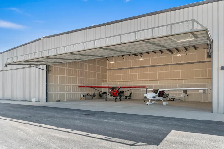 Spacious hangar with a wide bi-fold door, corrugated metal exterior, and interior lighting