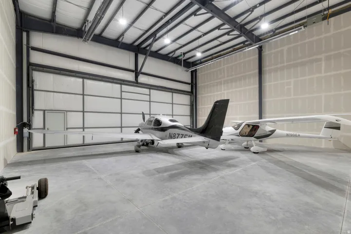 Spacious hangar featuring a large roll-up door, polished concrete flooring, exposed metal framing, and ample overhead lighting
