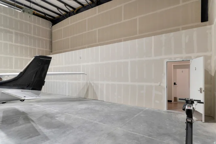 Concrete flooring, drywall walls, exposed ceiling joists, and an interior door