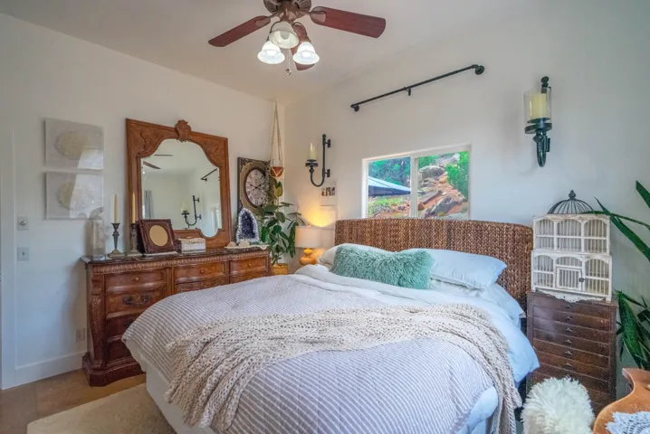 White walls with a ceiling fan, a window showcasing distant rock formations, and a woven headboard