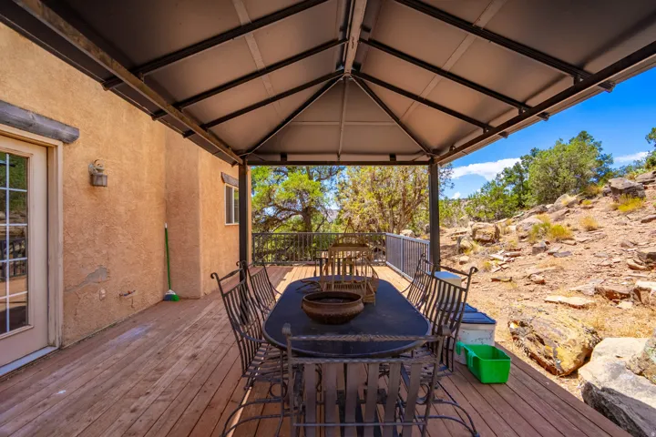 Covered deck with wood-finish flooring, stucco exterior, and surrounding natural rock landscaping