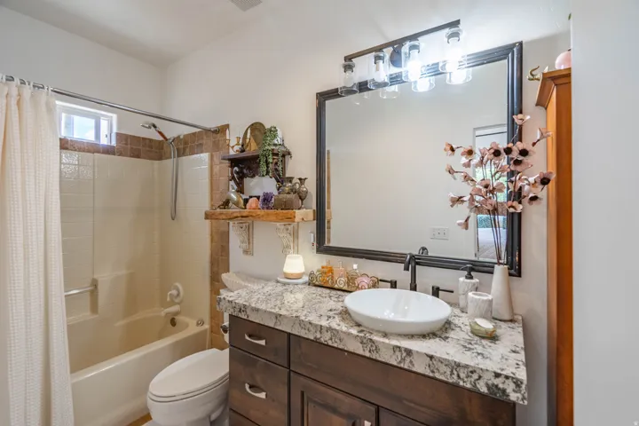 Bathroom featuring a wood-finish vanity with a stone countertop, a vessel sink, and a framed mirror