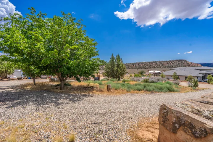 Expansive gravel area with mature trees and natural landscaping, set against a distant elevated landform