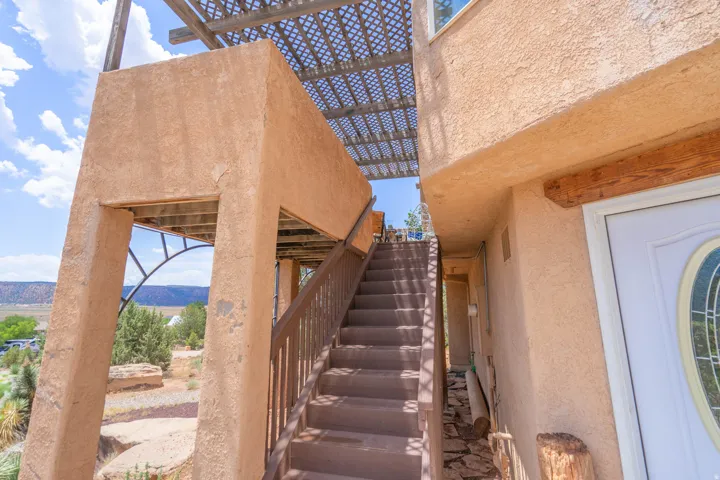 Stucco exterior featuring a wooden staircase, slatted overhead pergola, decorative wood beam, and an arched entryway