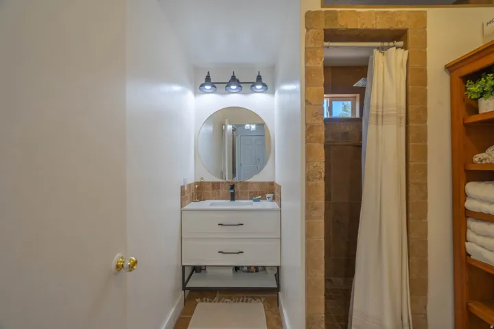 Vanity with white cabinetry and dark hardware, round mirror, and a three-light fixture