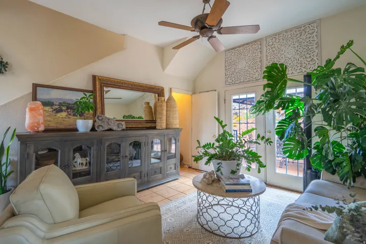 Bright, open living area featuring vaulted ceilings, ceiling fan, and abundant natural light from glass doors and windows