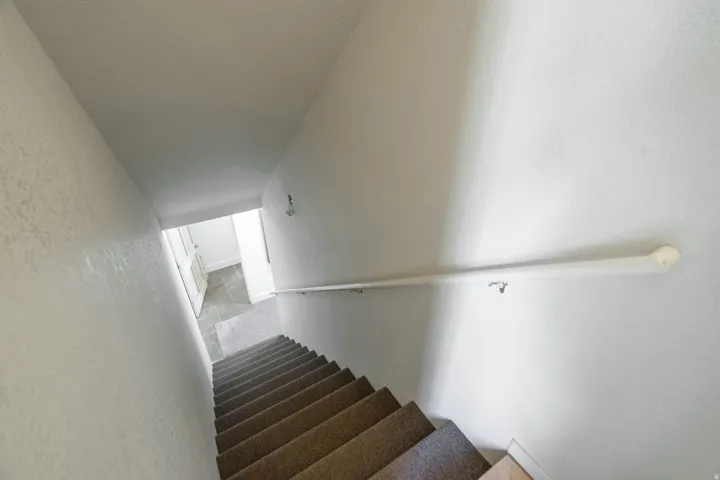 Staircase with wood-finish treads and metal handrail, illuminated by natural light from upper landing