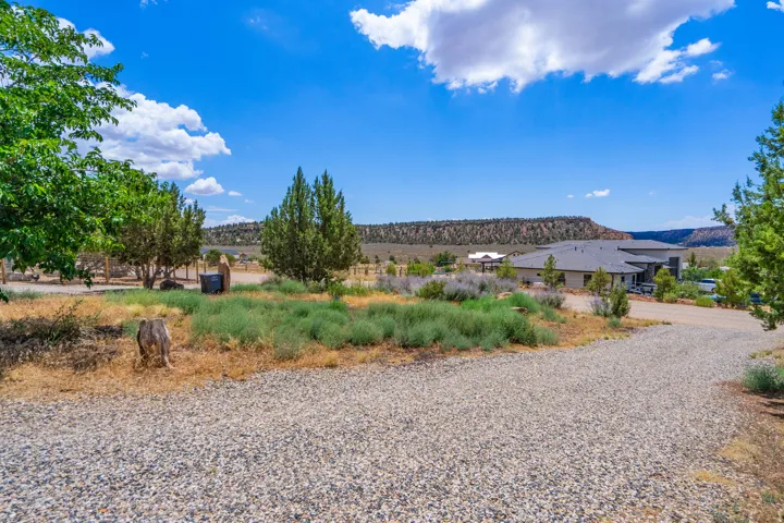 Gravel driveway leading to a contemporary residence with a dark-pitched roof, surrounded by natural landscaping and distant geological formations