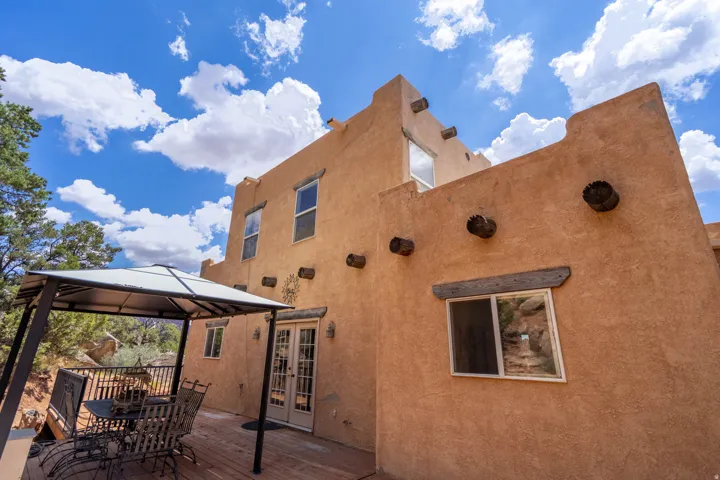 Stucco exterior with exposed wooden vigas, multiple windows, and a double glass door