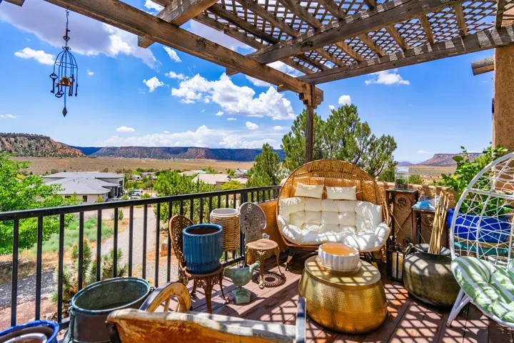 Expansive outdoor deck featuring a wooden pergola, black metal railing, and distant natural scenery