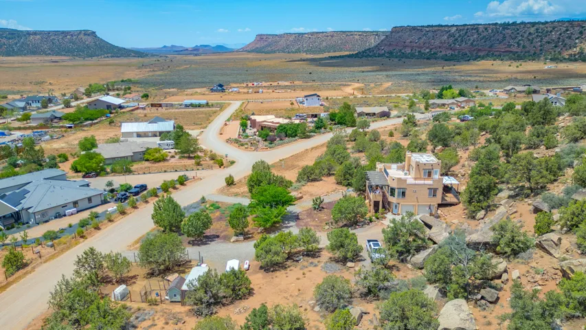 Southwestern-style architecture with multiple levels and a flat roof, elevated desert landscaping with mature trees, and a distant mesa backdrop