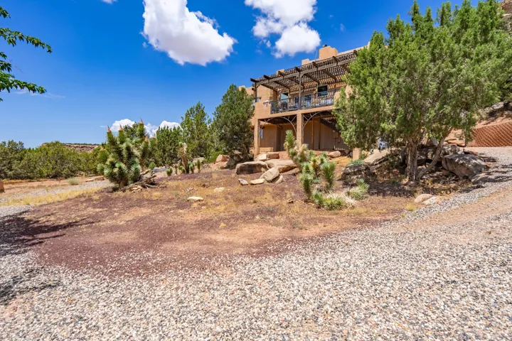 Southwestern-style residence with terracotta tile roofing and stucco exterior, situated on expansive grounds featuring native desert landscaping, mature evergreen trees, and gravel hardscaping