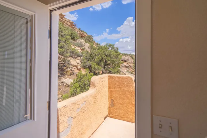 Expansive outdoor terrace with stucco-finished walls and direct access from interior living spaces, overlooking natural terrain with native vegetation and scenic hillside backdrop beneath clear skies