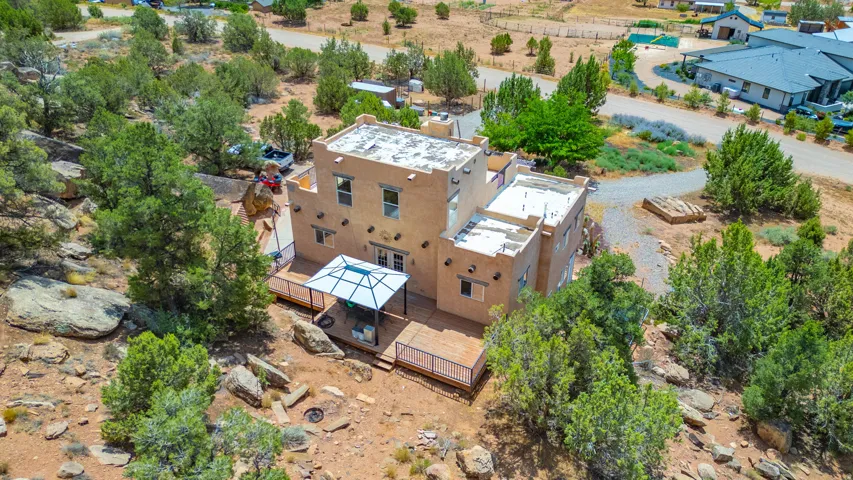 Adobe-style architecture with multi-level flat roofs, an expansive wood deck, and a white metal patio gazebo