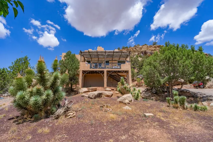 Multi-level exterior with a stucco finish, featuring a second-story balcony with a slatted pergola, and a lower-level arched entry
