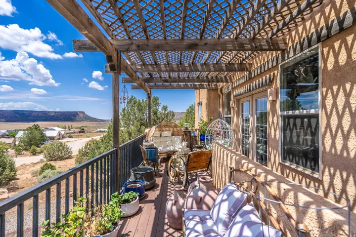 Expansive wood-finish deck with a pergola, black metal railings, double glass doors, and stucco exterior