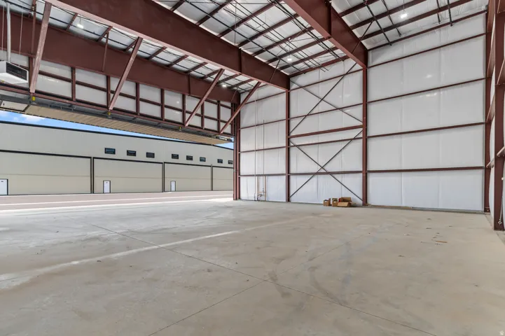 Expansive concrete flooring with high ceilings, exposed structural beams, and large hangar doors