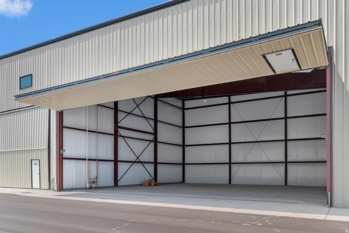 Metal-clad industrial building with a large hydraulic folding door, a secondary entry door, and a small upper-level window
