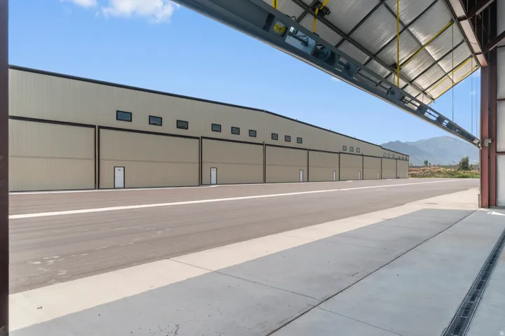 Expansive hangar facility with multiple bay doors, exterior windows, concrete pavement, and a wide tarmac