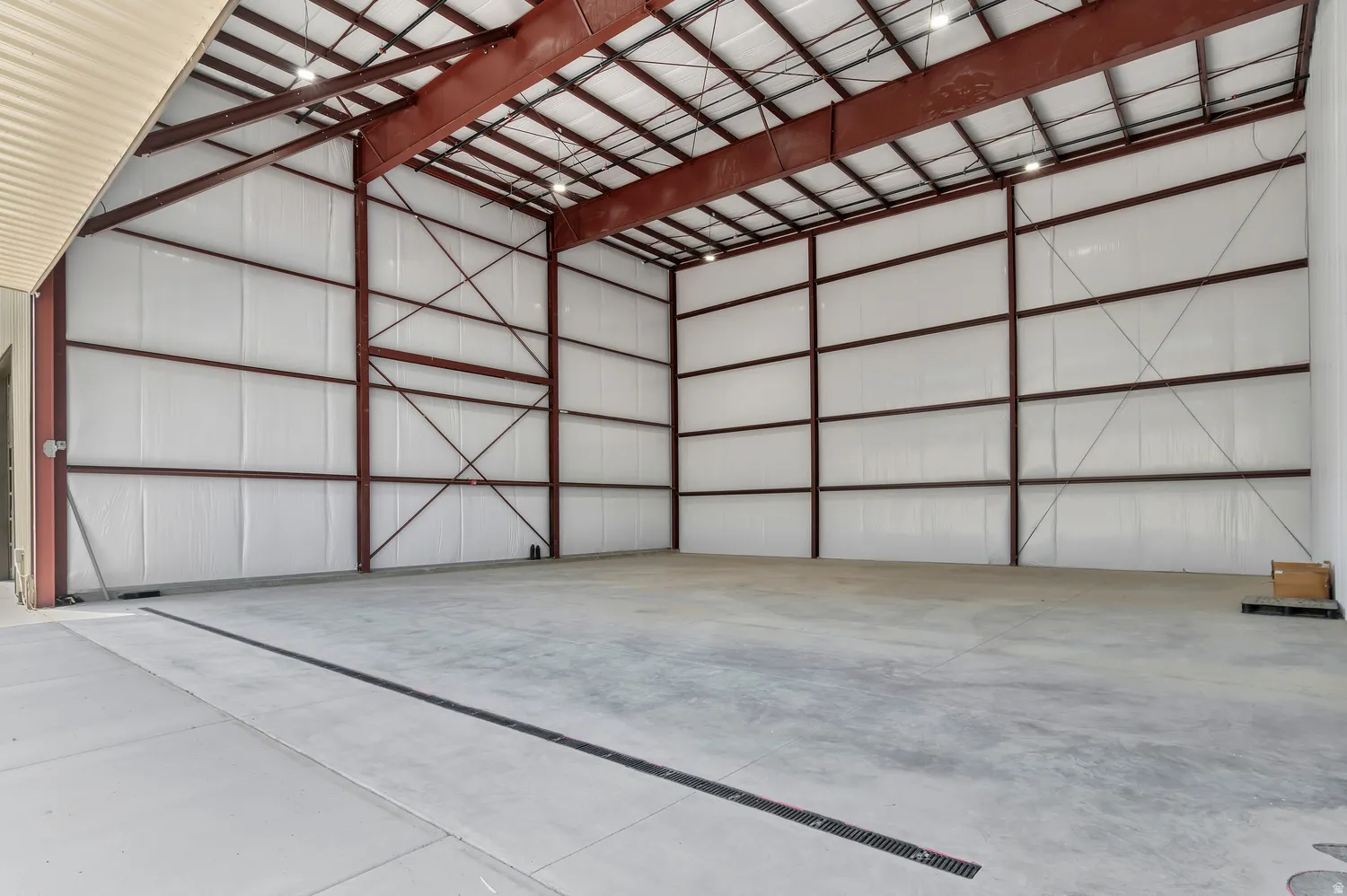 Spacious warehouse interior featuring a high ceiling, exposed steel structural beams, concrete flooring, and overhead lighting