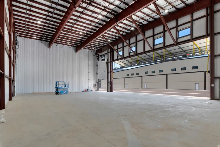 Expansive industrial space featuring a high truss ceiling, concrete flooring, and multiple overhead doors