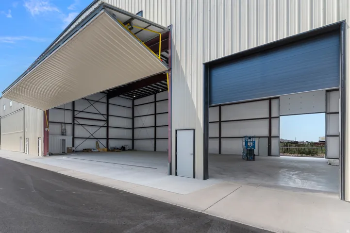 Large commercial building with a wide bi-fold hangar door, an additional roll-up door, and a personnel entry door