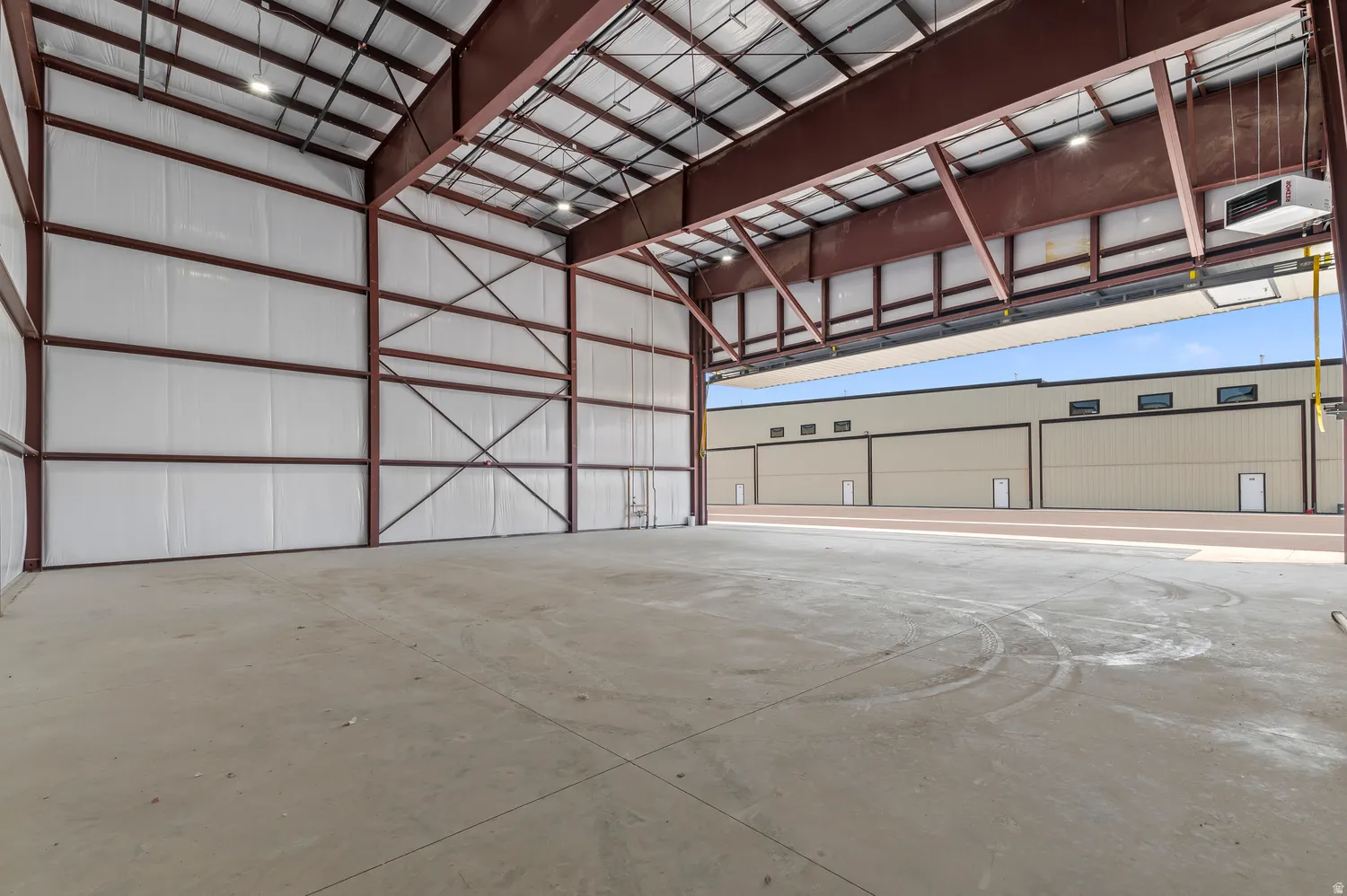 Spacious interior featuring a concrete floor, exposed metal structural beams, white insulated walls, and overhead lighting