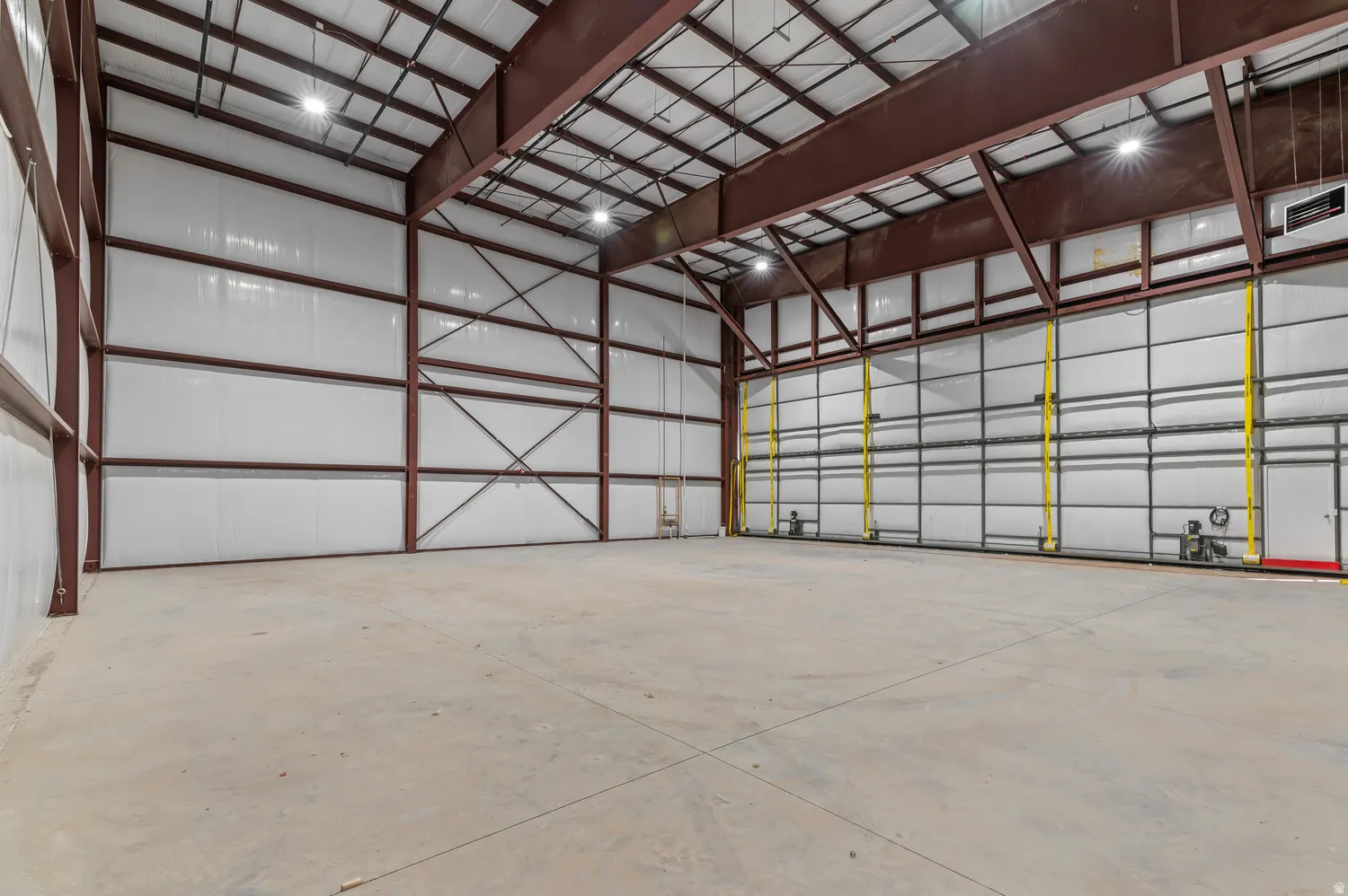 Expansive open interior with a concrete floor, exposed structural steel beams, and high ceilings with industrial lighting