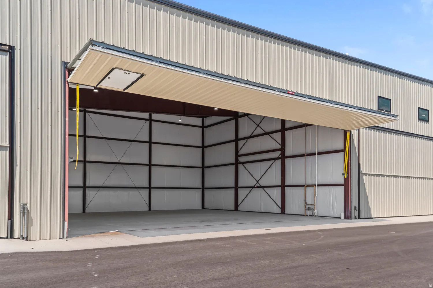 Metal-clad exterior with a large bi-fold hangar door, exposed steel structural beams, and a concrete floor