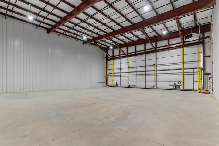 Expansive open warehouse space featuring a polished concrete floor, exposed metal beam ceiling structure, and multiple overhead doors