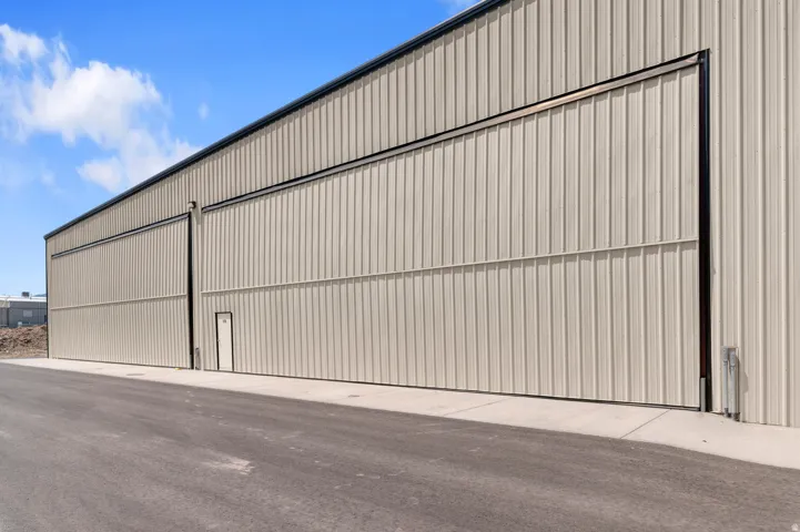 Corrugated metal exterior with multiple large sliding doors, a pedestrian entry, and a paved approach