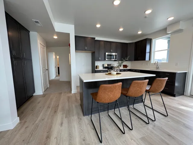 Kitchen featuring a central island with white countertop, dark wood-finish cabinetry, stainless steel appliances, and wood-finish flooring