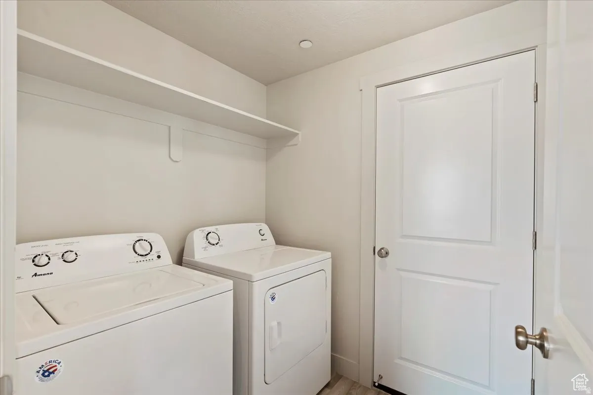 Dedicated laundry space featuring a white shelf, light wood-finish flooring, and a white panel door