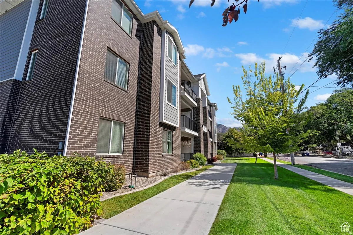 Modern brick townhome with a manicured front lawn, mature landscaping, and a wide concrete walkway