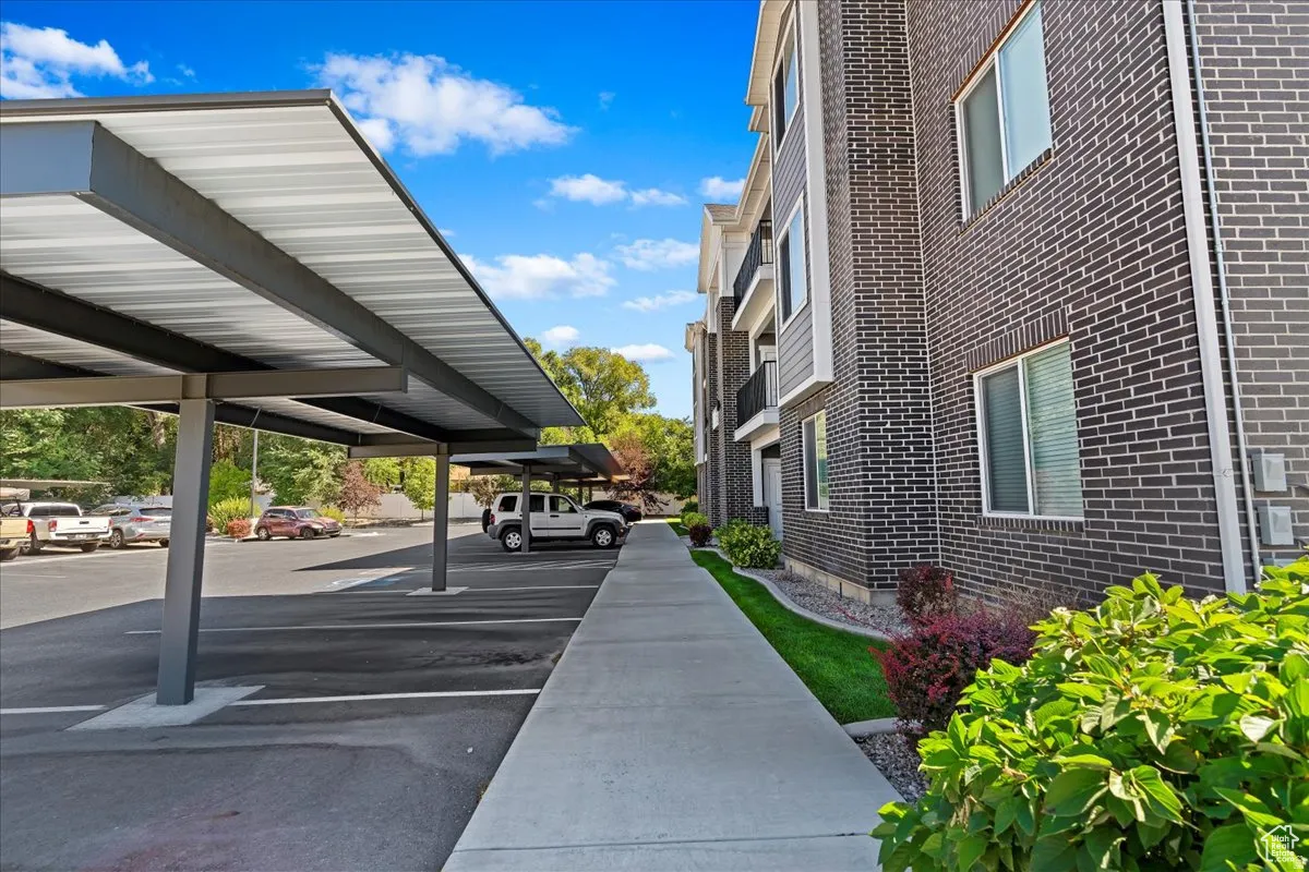 Carport parking with a paved lot, concrete pathway, brick exterior, and landscaped grounds