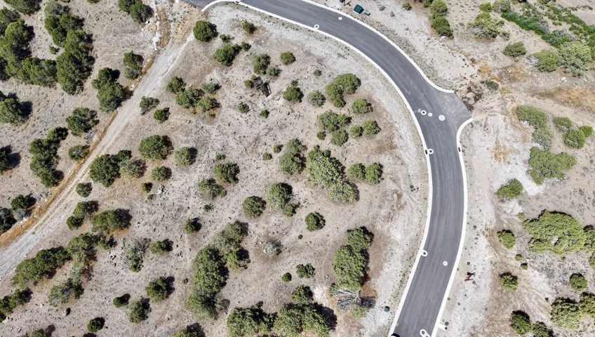 Curved asphalt road with defined shoulders, surrounded by arid terrain and scattered evergreen shrubs