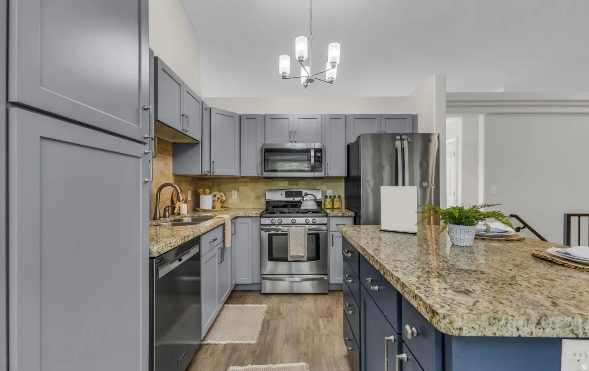 Kitchen featuring gray cabinetry, stainless steel appliances, granite countertops, wood-finish flooring, and a central island with blue cabinetry