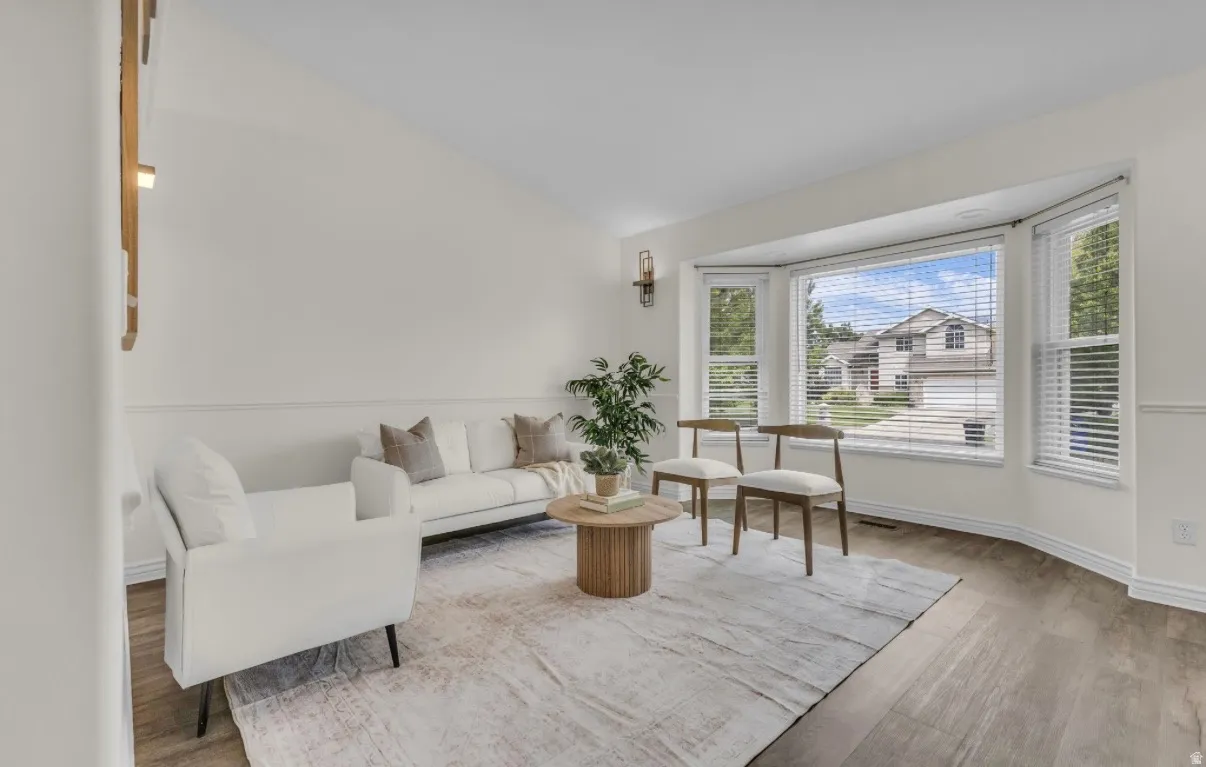 Vaulted ceiling living space with a large bay window, wood-finish flooring, and decorative wainscoting