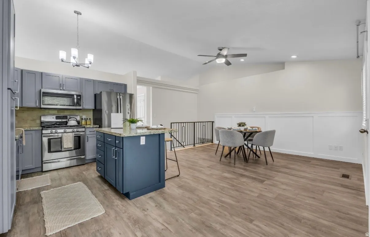 Open-concept kitchen with wood-finish flooring, stainless steel appliances, blue cabinetry, and a central island with a granite-style countertop