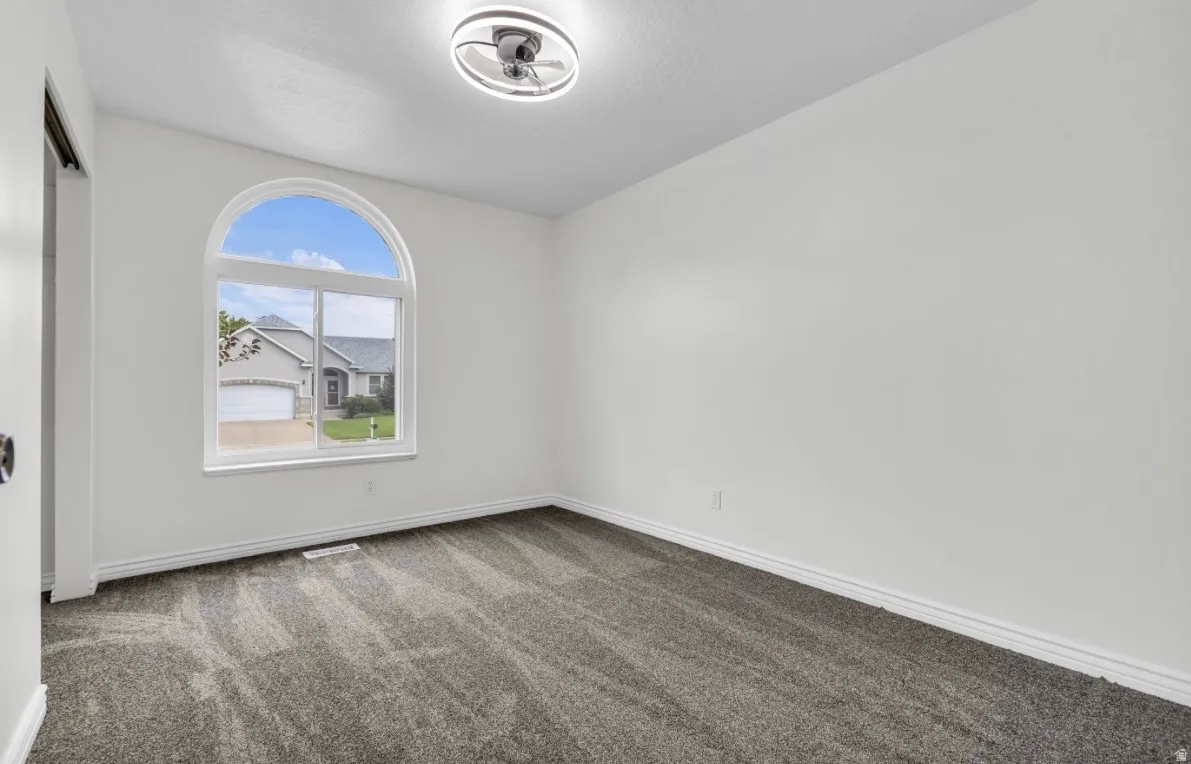 Arched window with white trim, gray patterned carpeting, white walls, and a modern ceiling light fixture