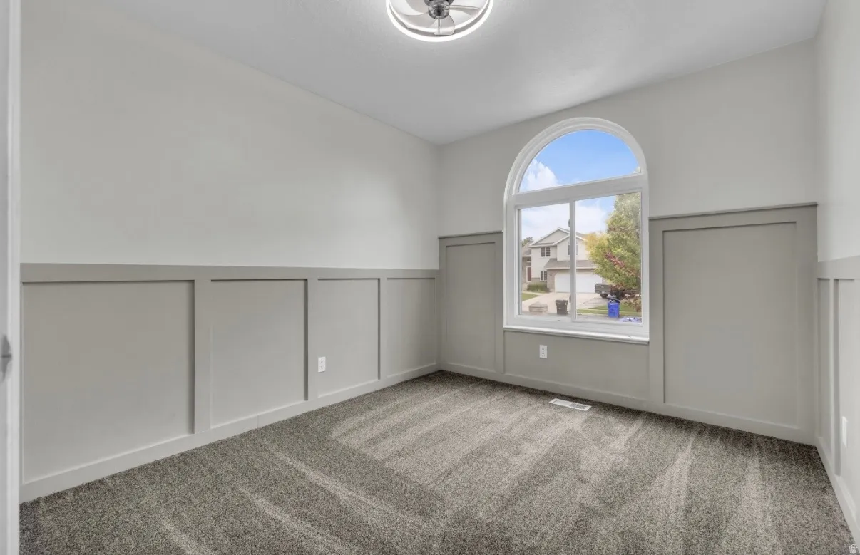 Bright, light-filled room featuring an arched window with natural light, neutral wall finishes with wainscoting detail, and patterned carpet flooring