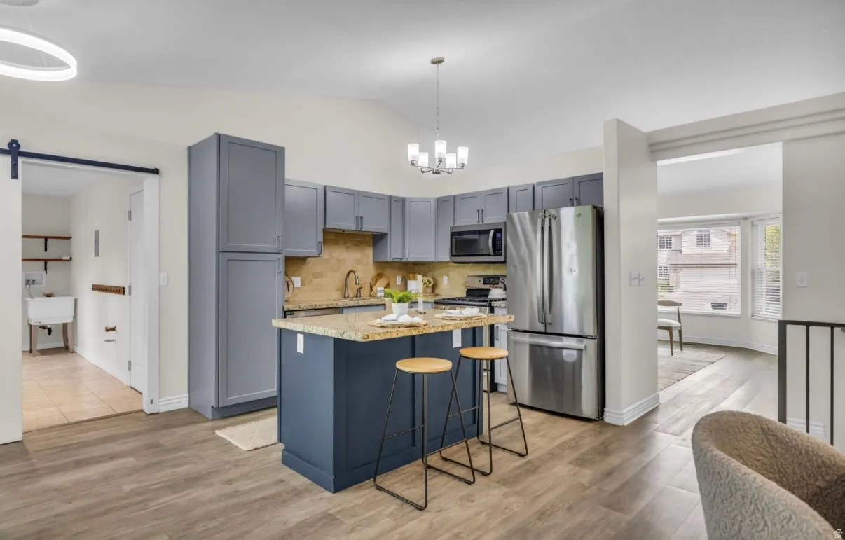 Vaulted ceiling, wood-finish flooring, blue cabinetry, stainless steel appliances, and a kitchen island with seating