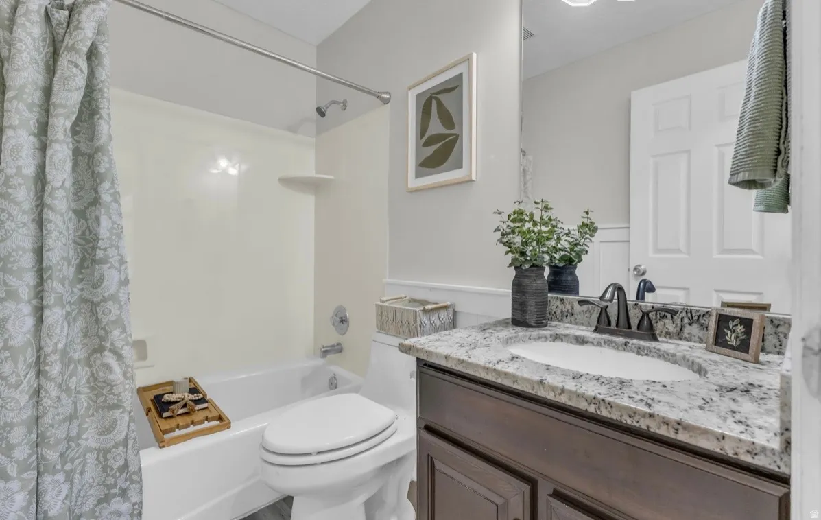 White bathtub with a shower, dark wood-finish vanity with a stone-finish countertop, and a white porcelain toilet