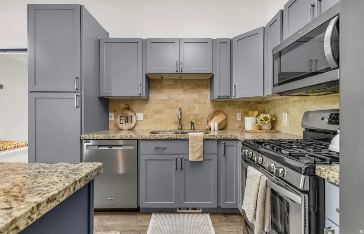 Kitchen featuring gray cabinetry, stone countertops, stainless steel appliances, a tile backsplash, and wood-finish flooring