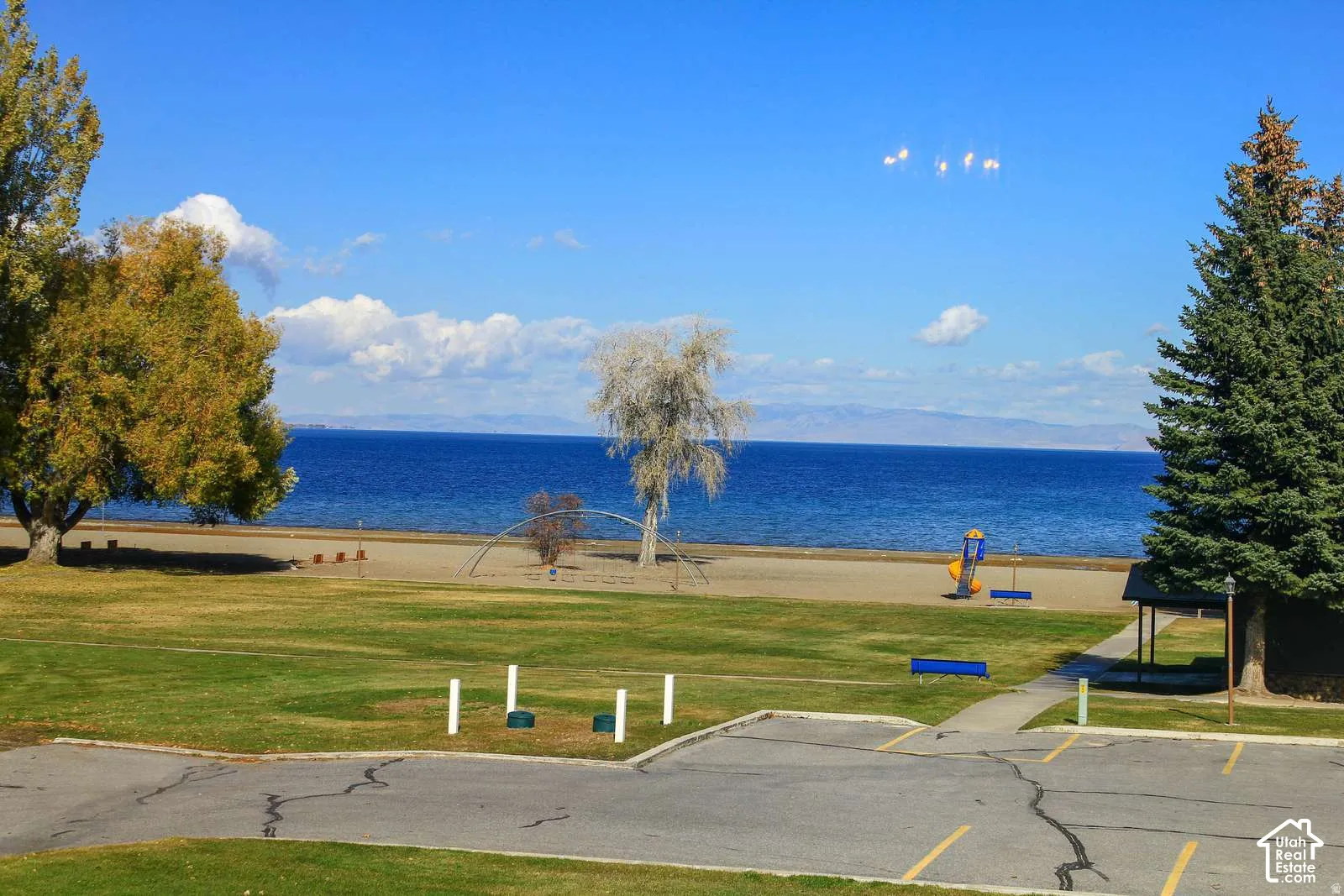 Waterfront property featuring expansive manicured lawn with mature trees, direct beach access, and panoramic water vistas