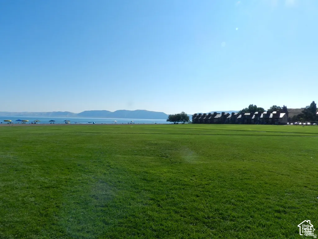 Expansive green lawn bordering a body of water with distant mountains and a row of residential structures