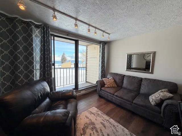 Sliding glass door leading to an exterior balcony, dark wood-finish flooring, overhead track lighting, and a textured ceiling finish